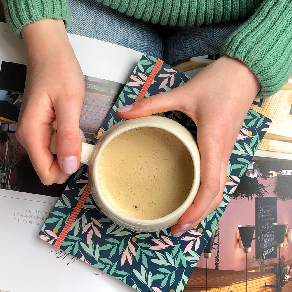 woman holding a coffee on top of a notebook and a magazine