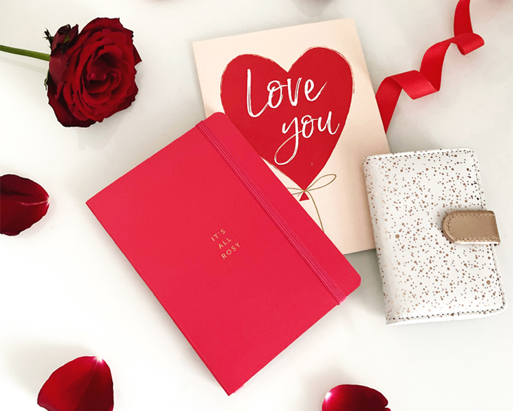 Red A6 Notebook, Valentine's Card and a Card Overspill Book surrounded by a rose, red rose petals and red ribbon. Valentine's Gift Ideas
