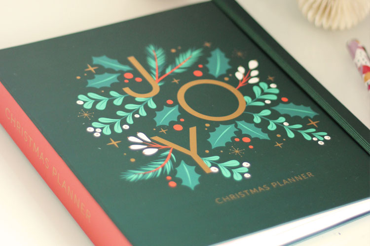 Close up shoot of our Christmas Planner with a green cover, red spine and festively decorated with holly and leafs with the word "JOY" in gold. Part of our new stationery launch